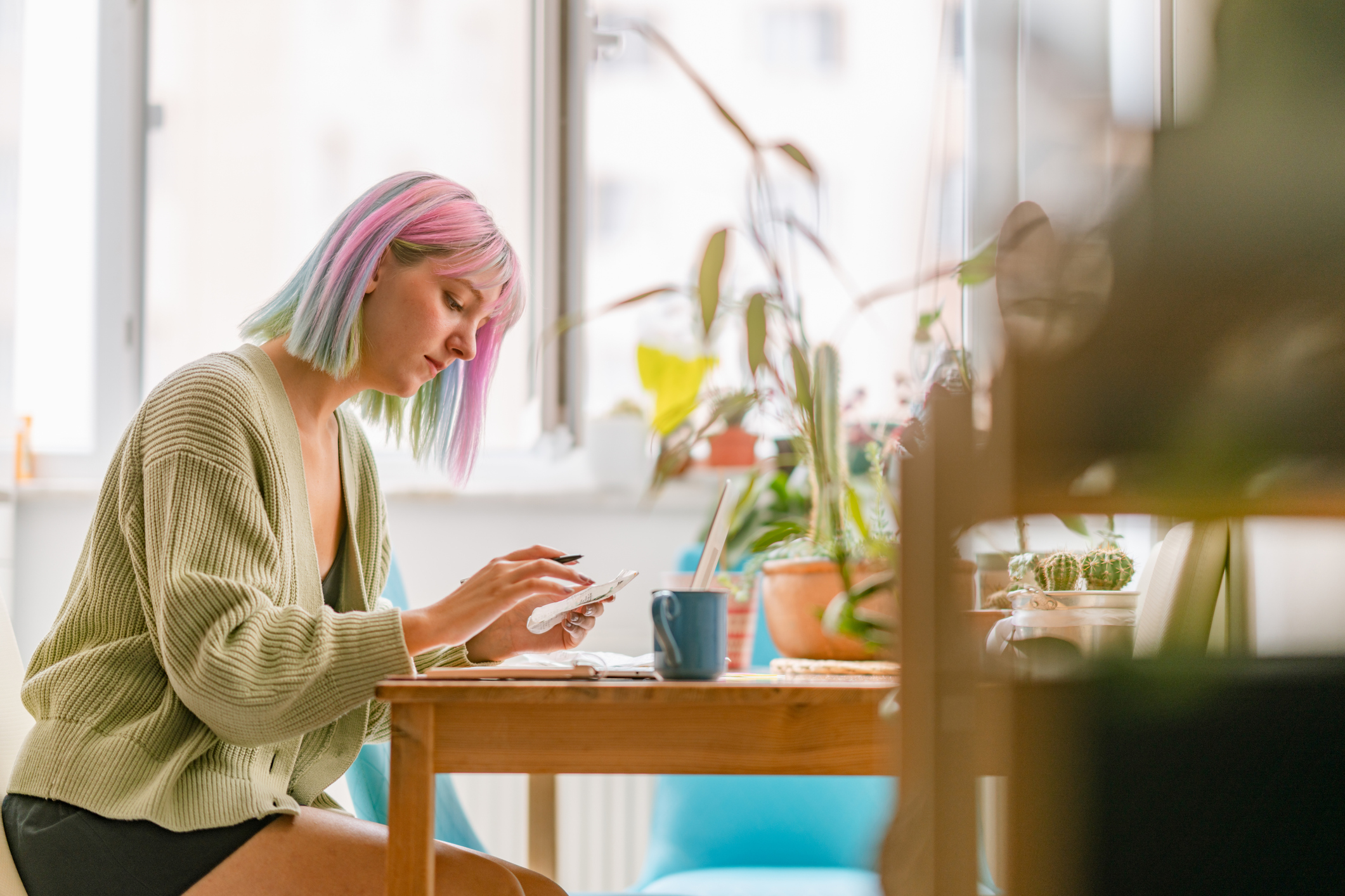 Woman with pink hair checking receipts at dining table