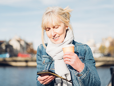 Woman looking at a phone while drinking coffee outdoors