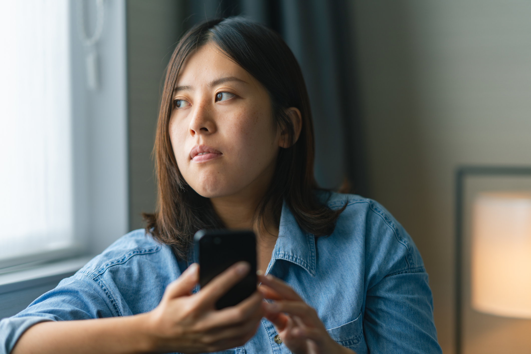 Woman looking out window while holding phone