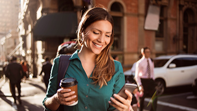 Woman smiling and looking at phone with coffee in hand