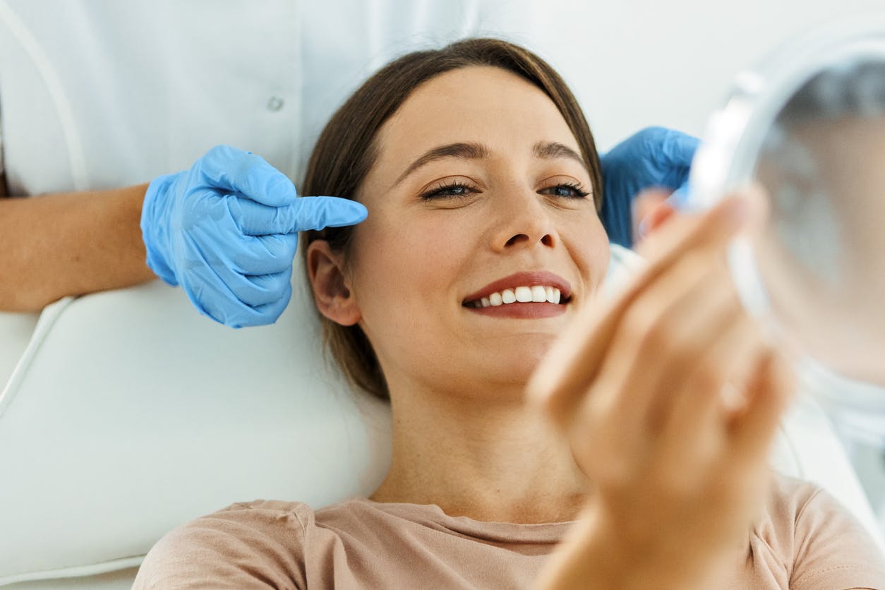 A woman in exam chair looking into hand mirror