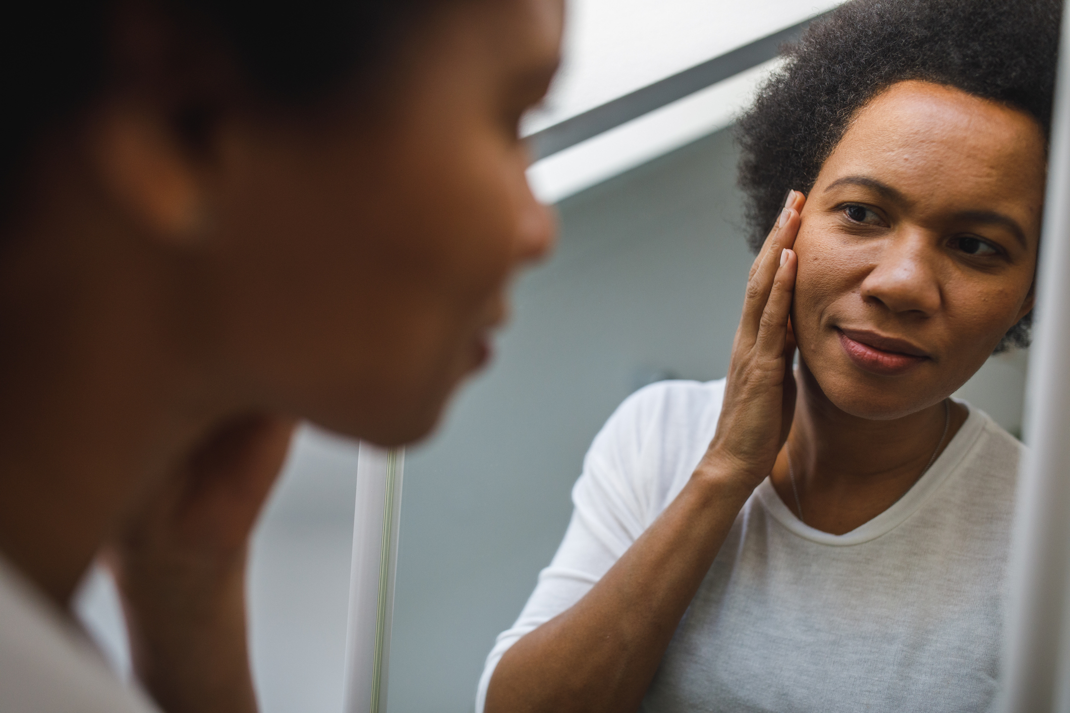 Person looking at their reflection while touching one side of their face.