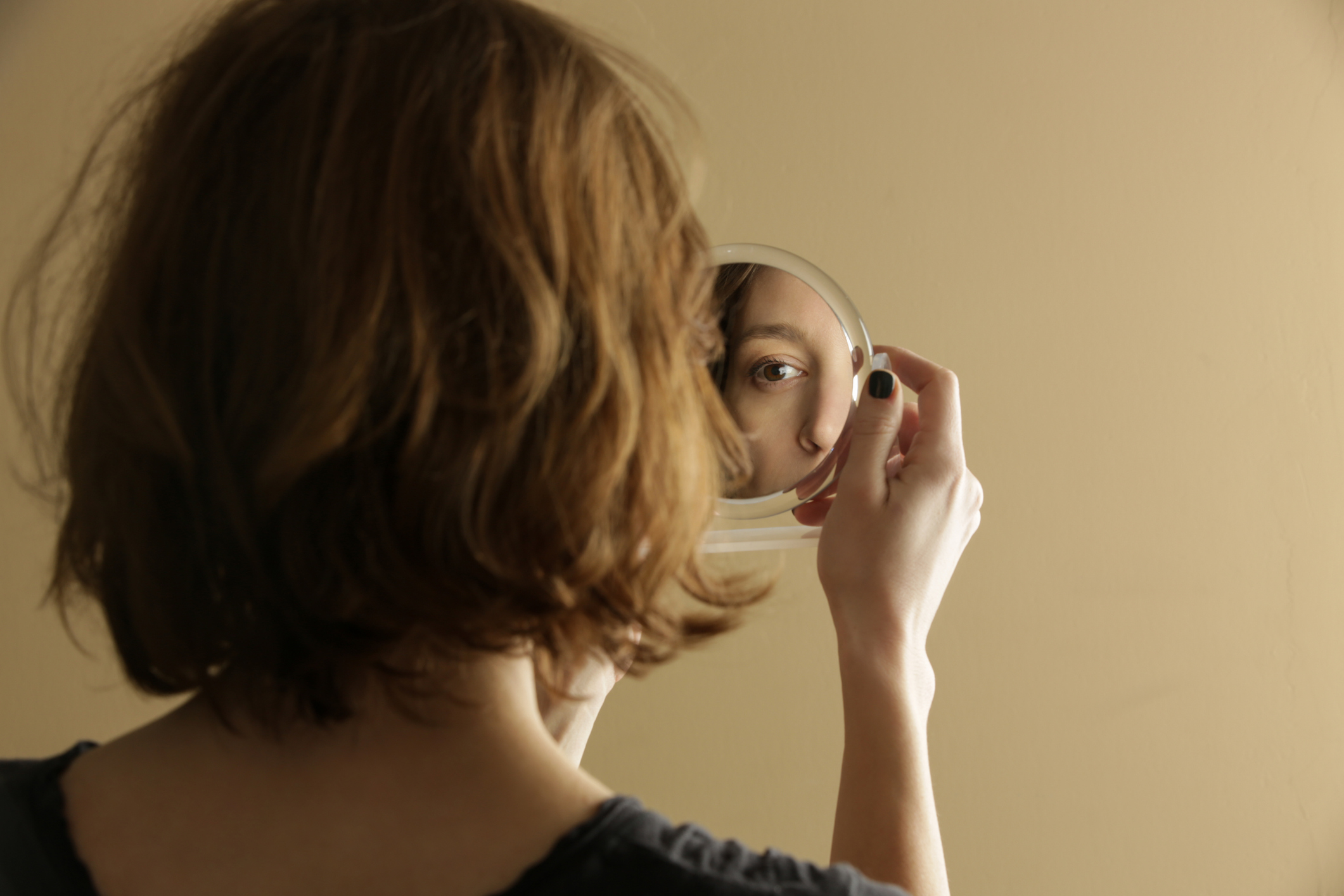 Woman examining her eye in a handheld mirror.