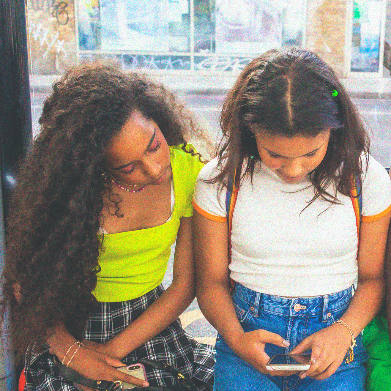 2 teen girls looking at phone at a bus stop