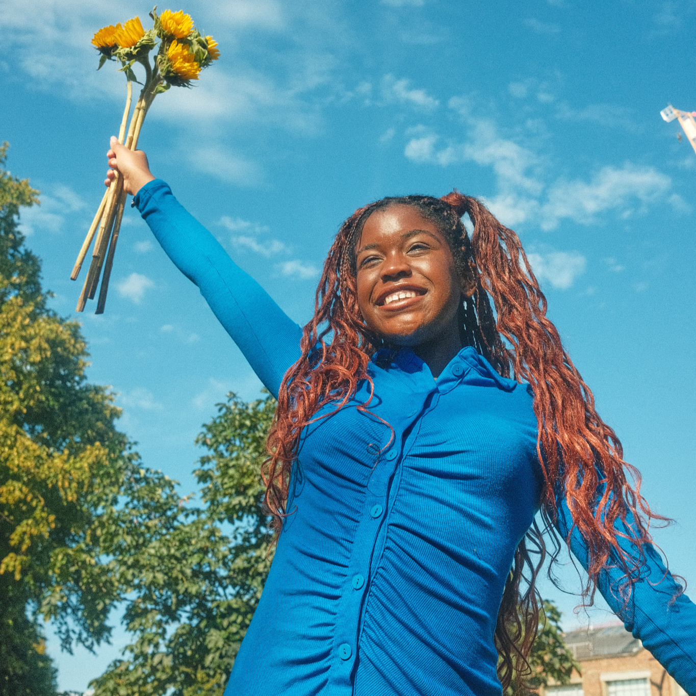 girl holding sunflowers in the air with a beaming smile