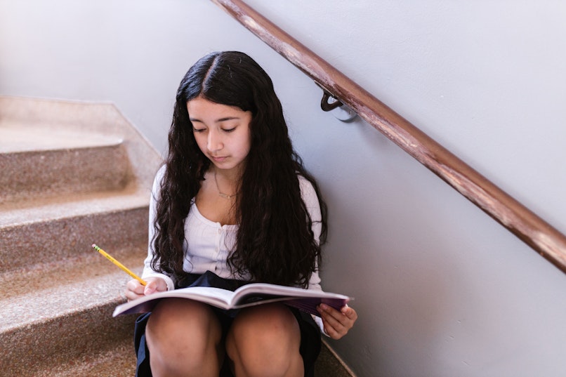 A girl sits alone on a staircase writing in a notebook.