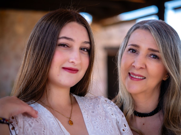 A teenage girl and an older woman pose close together smiling for a portrait, with the woman's hand on the girl's shoulder.