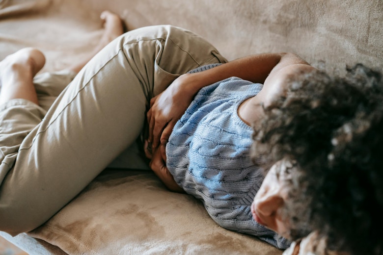 A girl lies curled up on a couch holding her stomach.