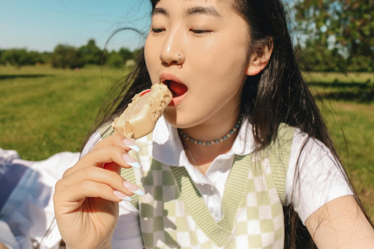 Teenage girl eating an ice lolly outdoors in a field, wearing a green checked vest.