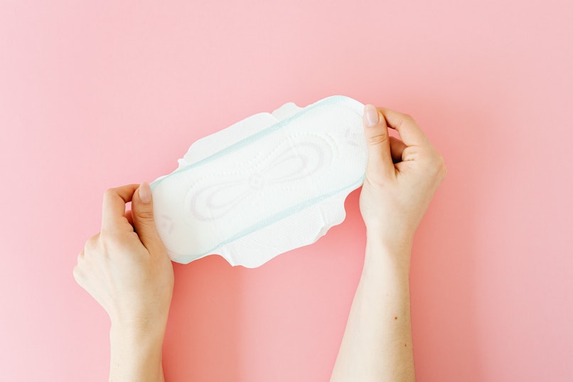 Two hands holding a period pad against a pink background.