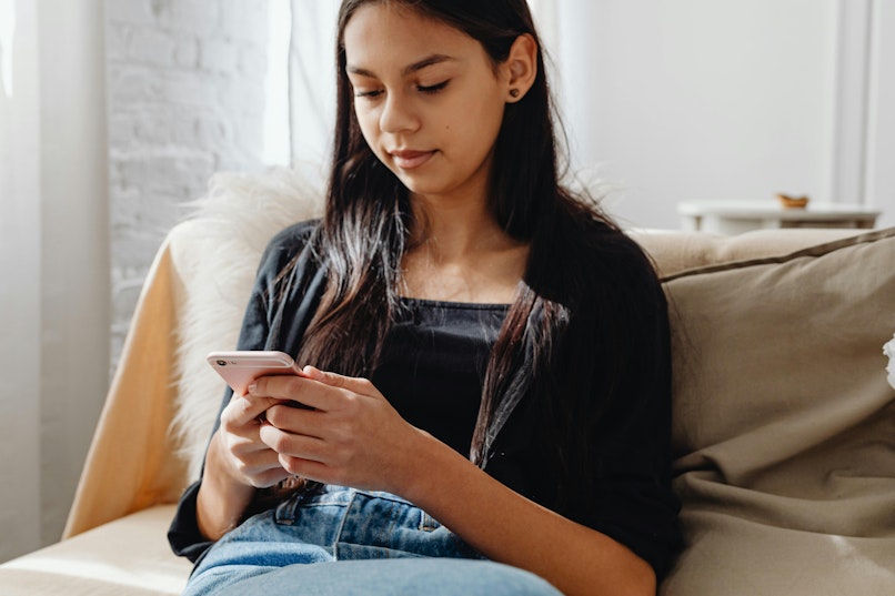 Teenage girl sitting on a sofa looking down at her phone.