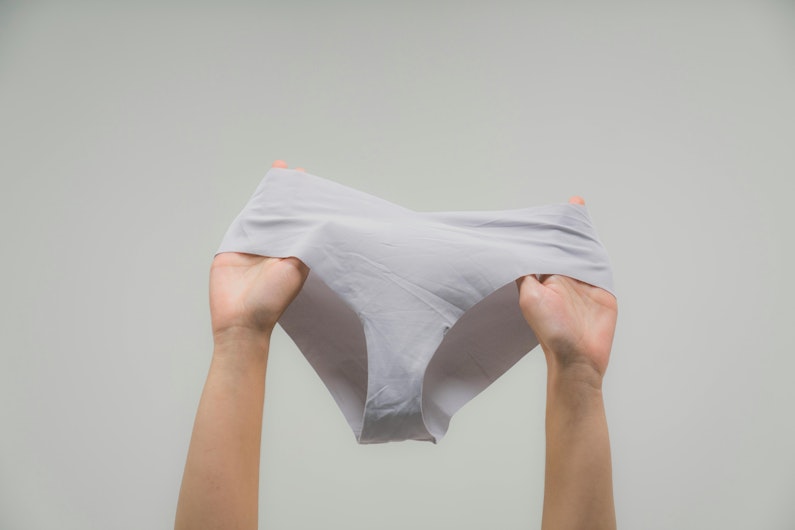 Two hands hold up a pair of grey underwear against a plain background.