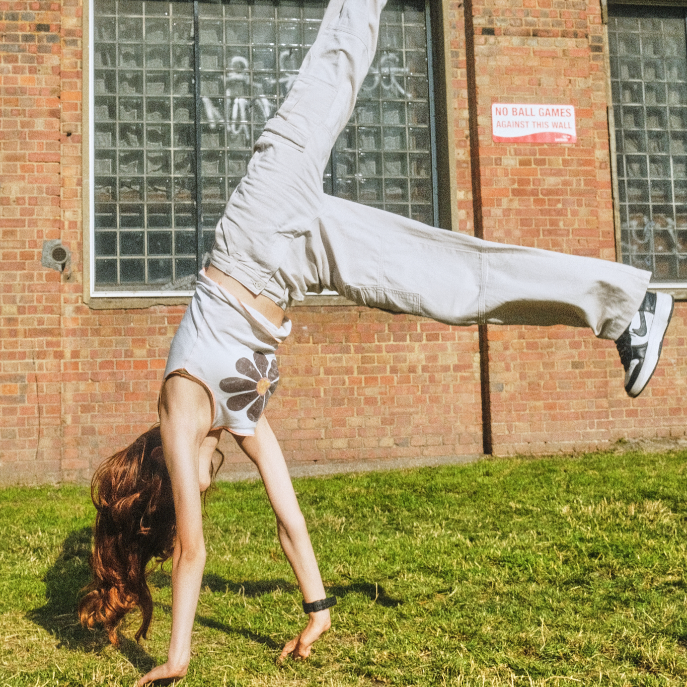 Teenage girl with long hair doing a cartwheel on grass in front of a brick building.