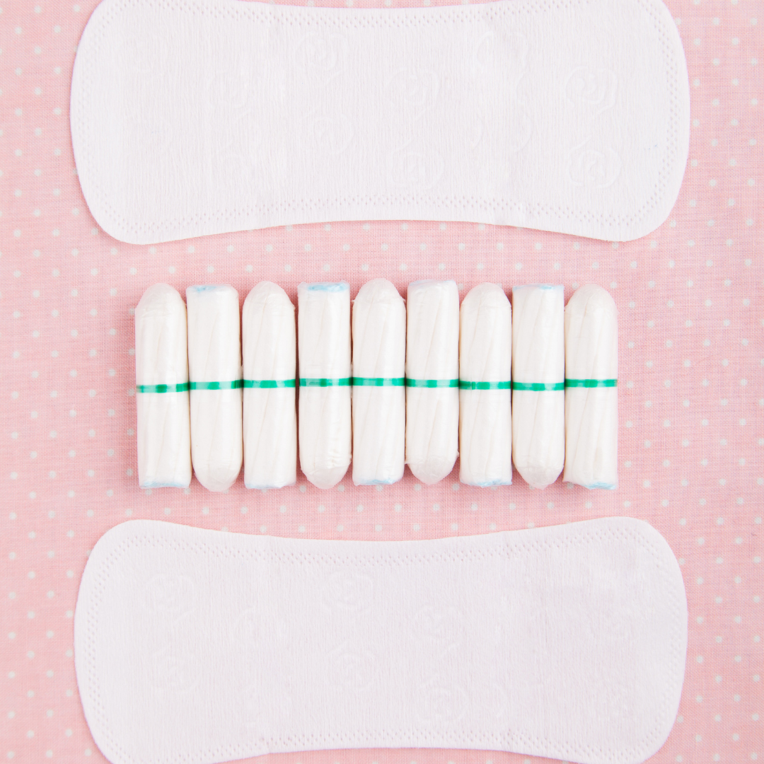Flat lay of period pads and tampons with green string, arranged in rows on a pink polka-dot background.