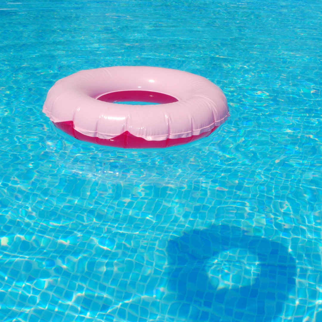 A pink inflatable ring float sits in a bright blue swimming pool.