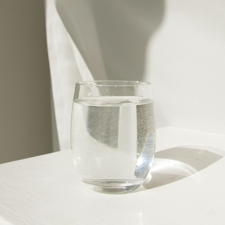 A glass of water catching sunlight on a white table against a neutral background.