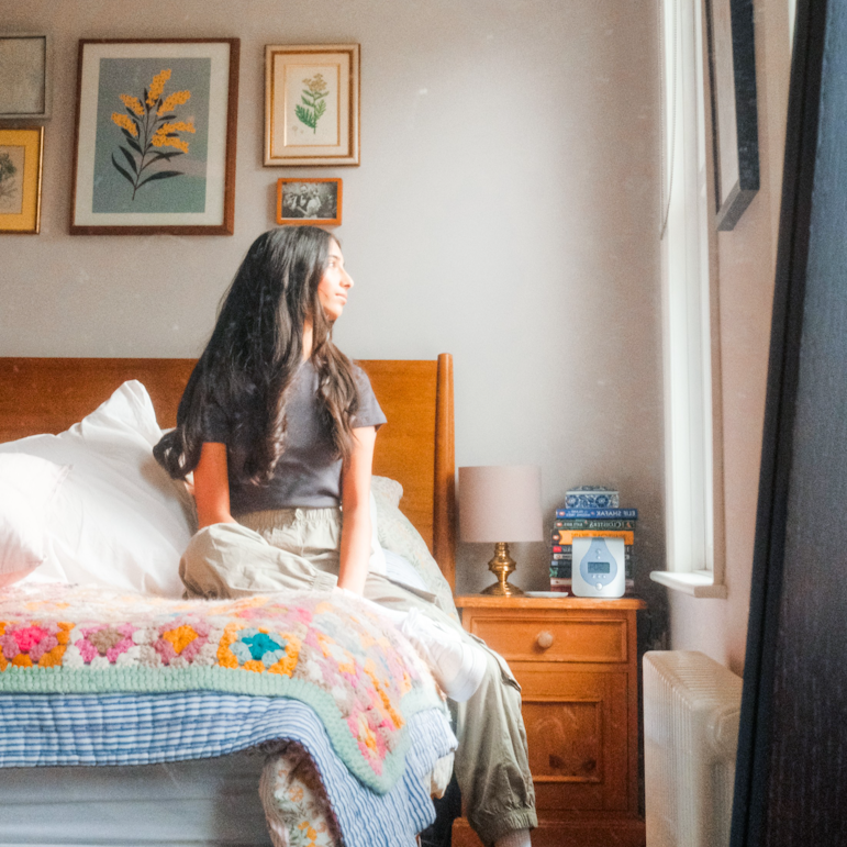 Teenage girl sitting on a bed looking out of the window in a cosy bedroom decorated with framed prints.