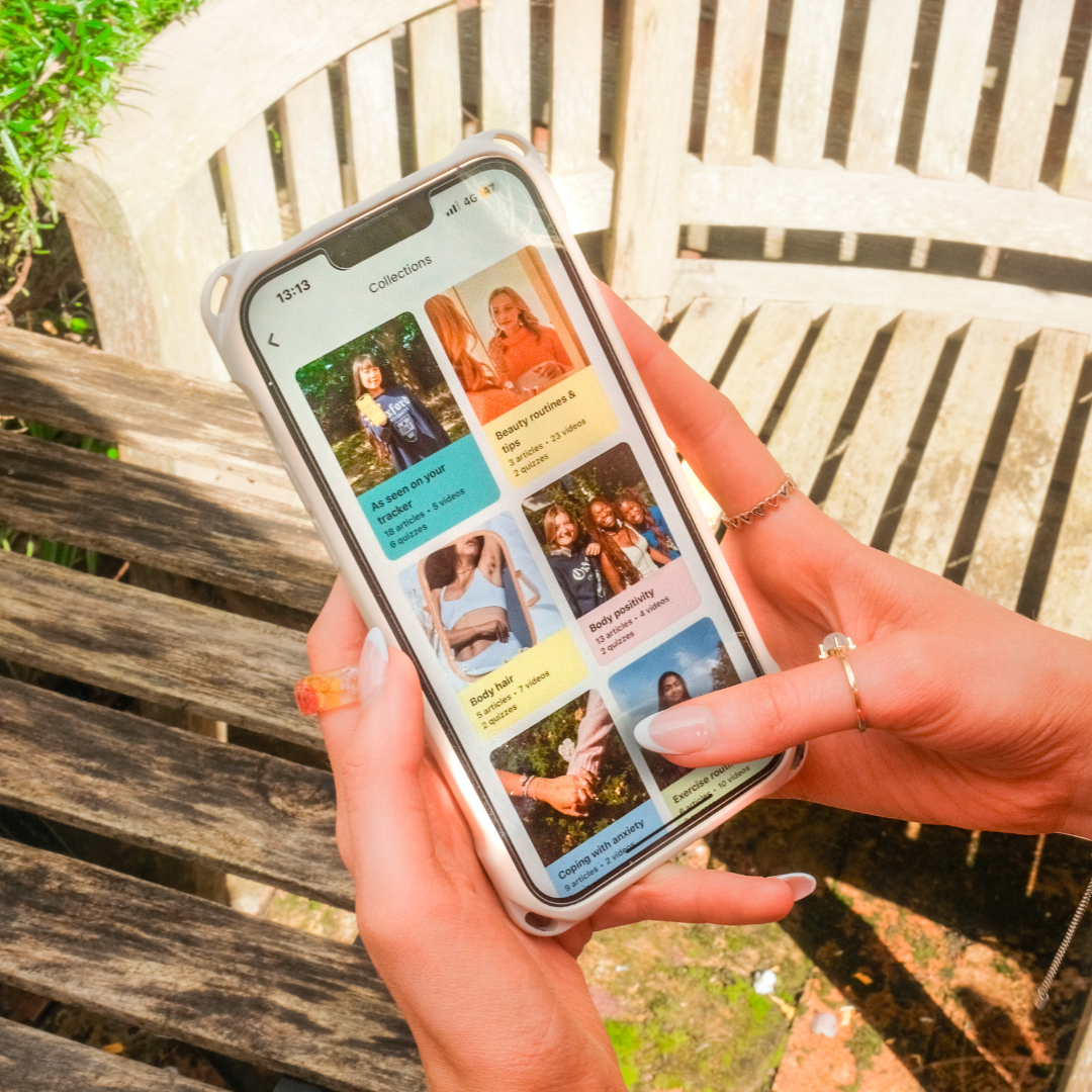 Hands holding a phone outdoors showing the luna app's collections screen with several video categories, including body positivity and beauty tips.