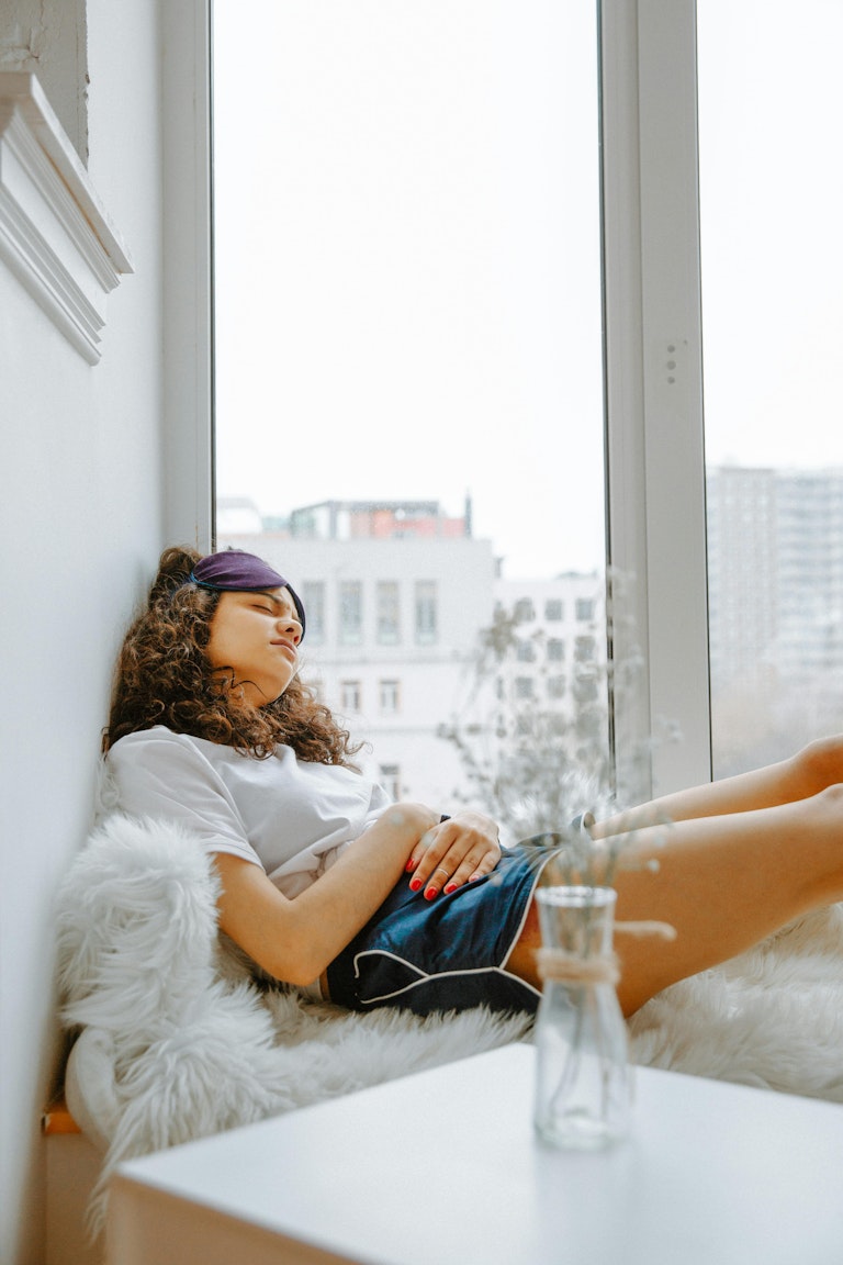 Girl with curly hair relaxing on a cushioned windowsill with her hands resting on her stomach.