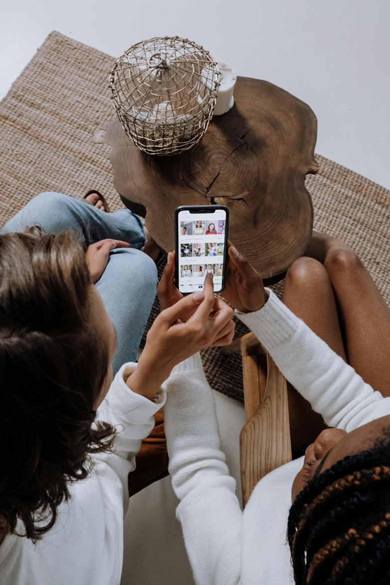 Two people sitting on the floor looking together at a phone showing a grid of photos.