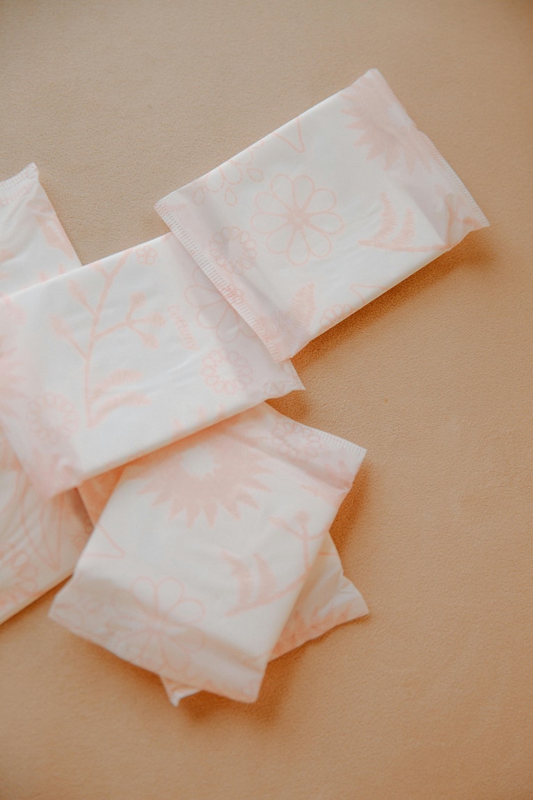 Several individually wrapped period pads with a soft floral pattern laid out on a peach background.