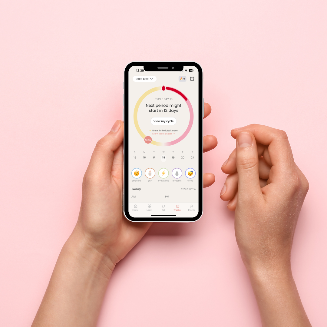 Hand holding a phone showing the luna app's cycle tracker with days until next period and a calendar view, against a pink background.