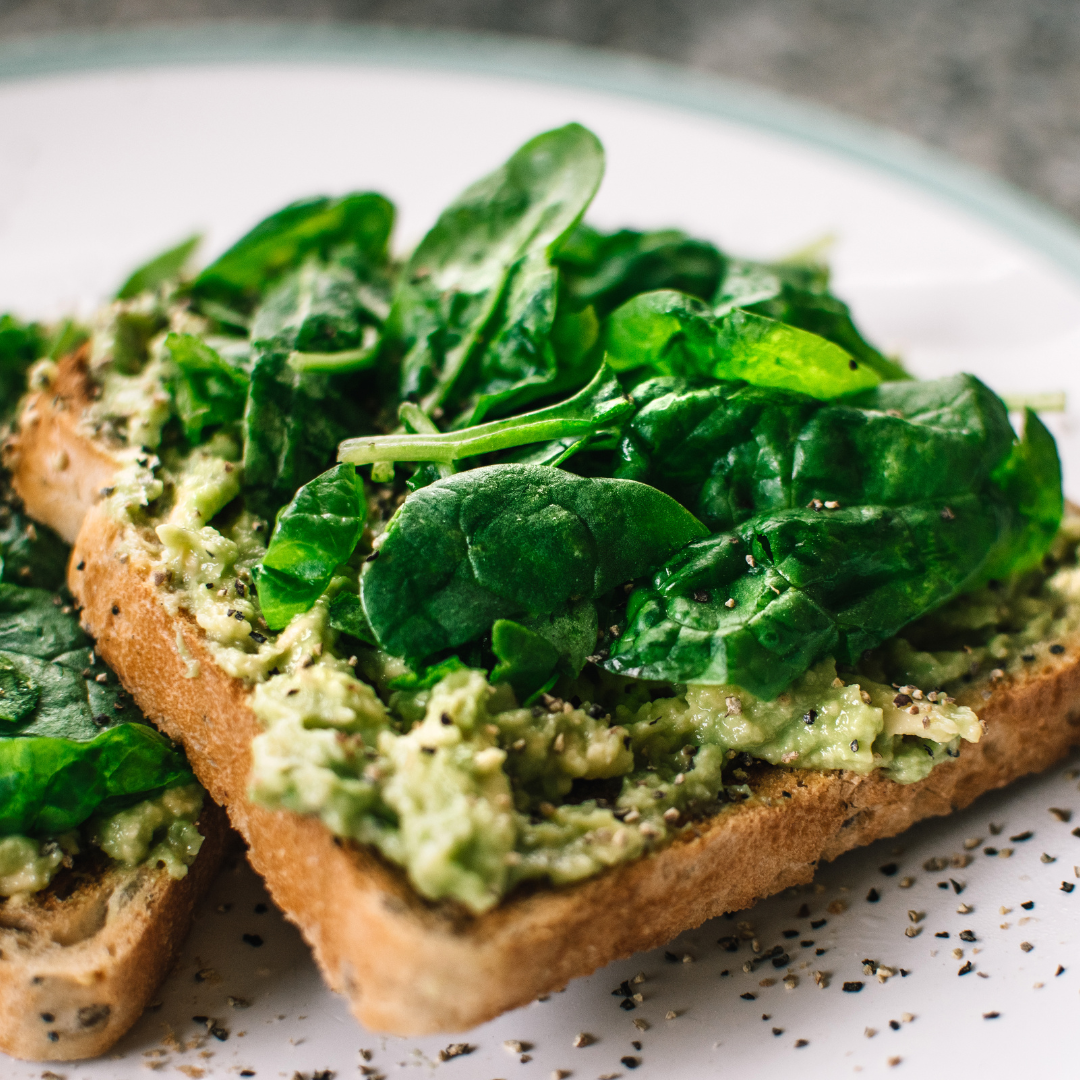 Two slices of toast topped with mashed avocado, fresh spinach leaves and black pepper on a plate.