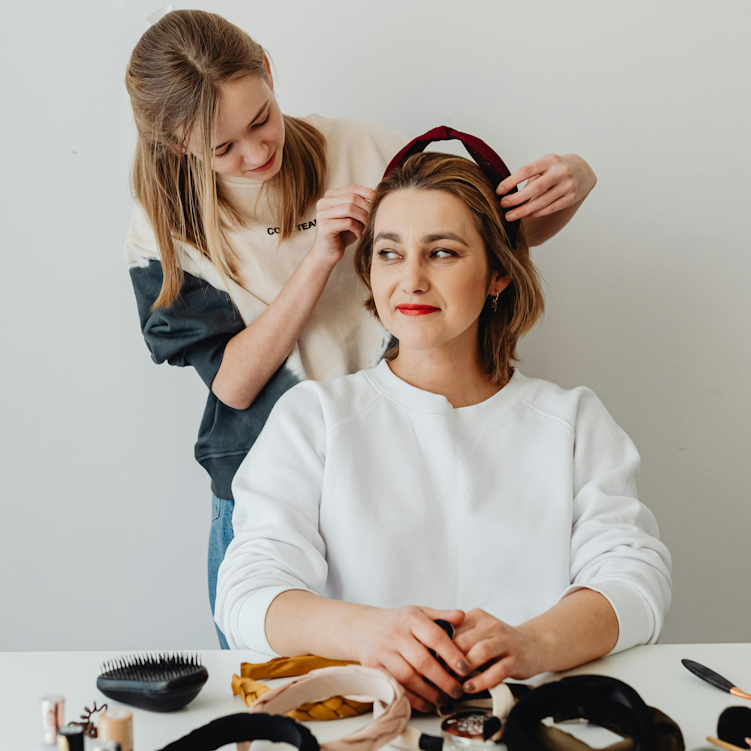 Teenage daughter fastening a headband into her mum's hair, with hair accessories laid out on the table in front of them.