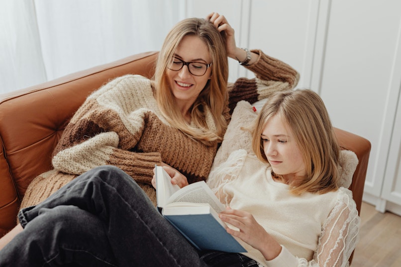 Mother and daughter sitting together on a sofa, reading a book together.