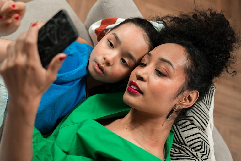 Mother and son lying together on a sofa, looking at a phone she's holding up.
