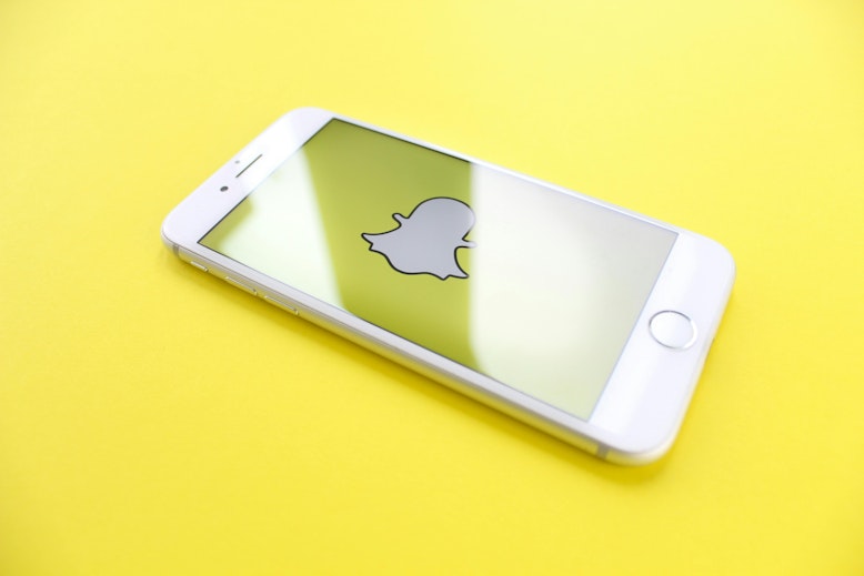 Phone lying on a yellow background displaying the Snapchat logo on its screen.