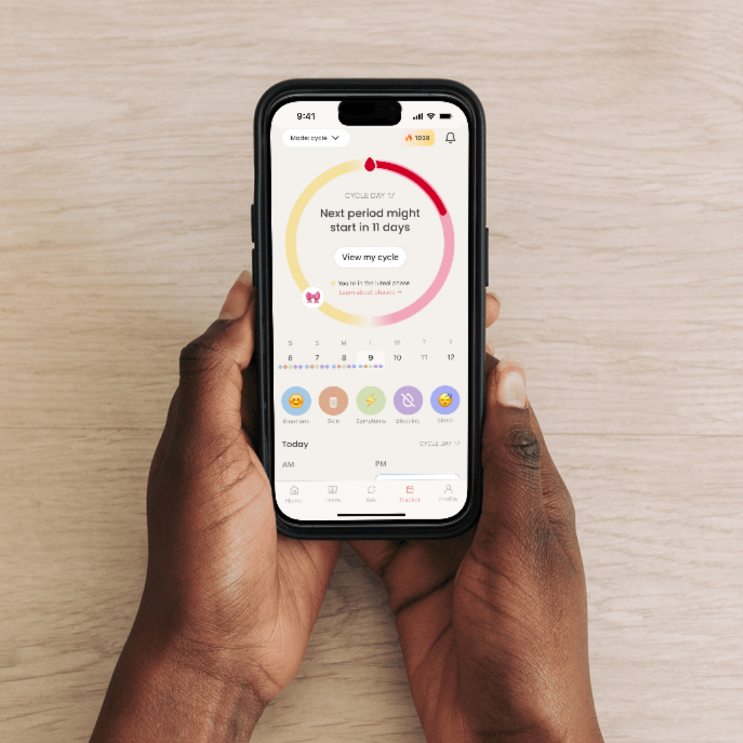Hands holding a phone showing the luna app's cycle tracker with days until next period and a calendar view.