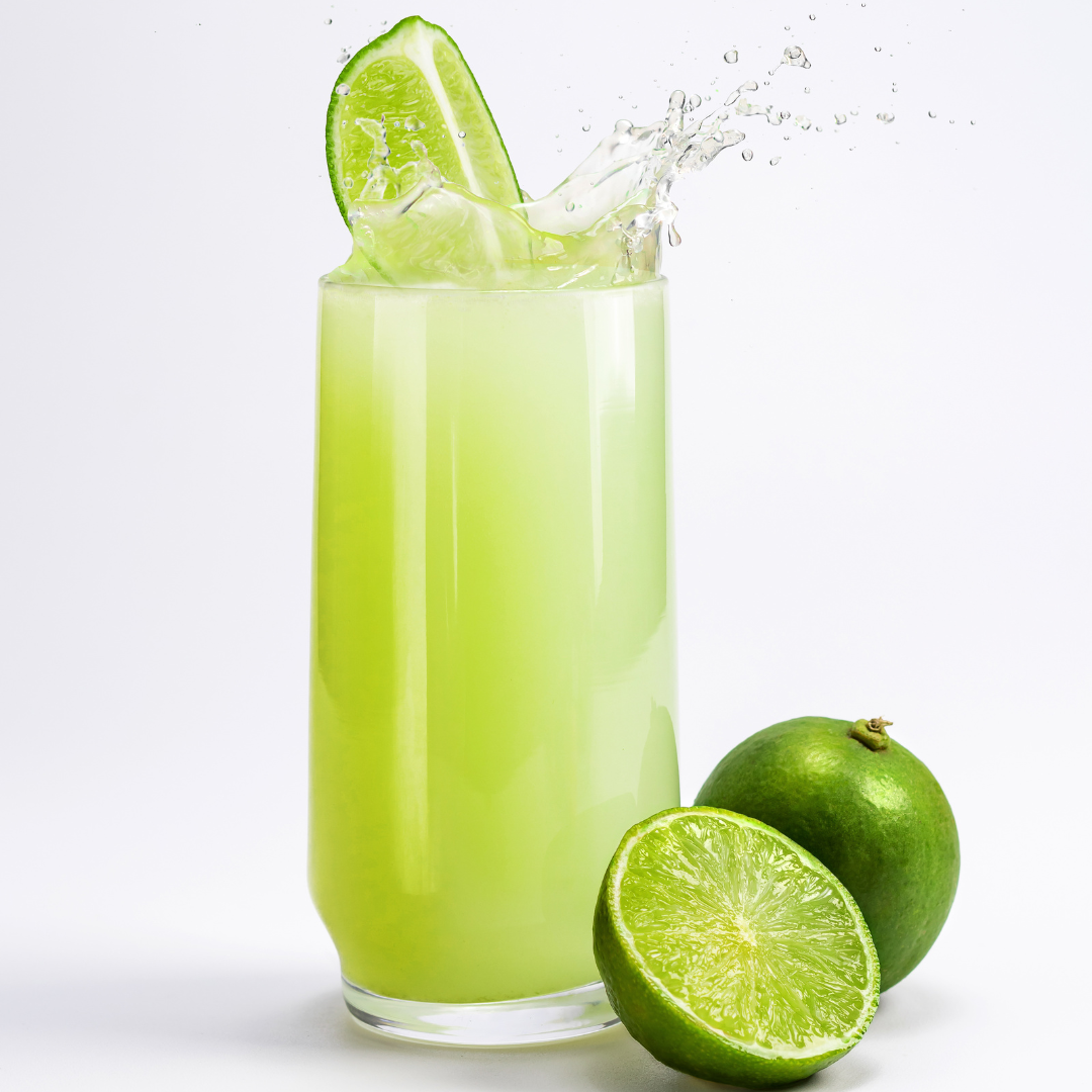 Glass of green lime juice splashing with lime slices on top, next to whole and halved limes.