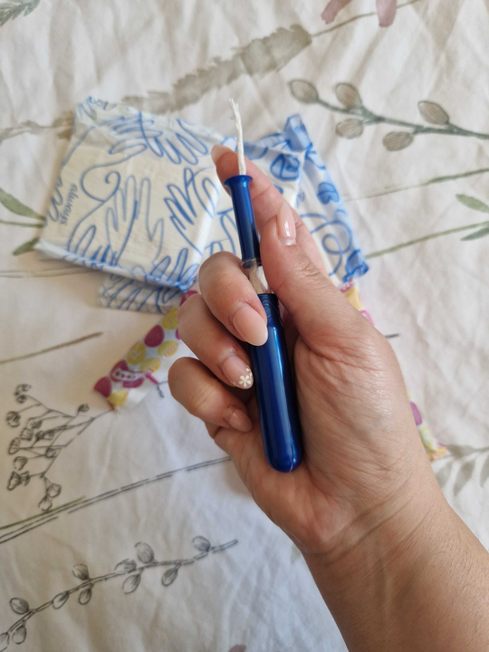 Hand holding a tampon with period pads laid out on a patterned bedspread in the background.