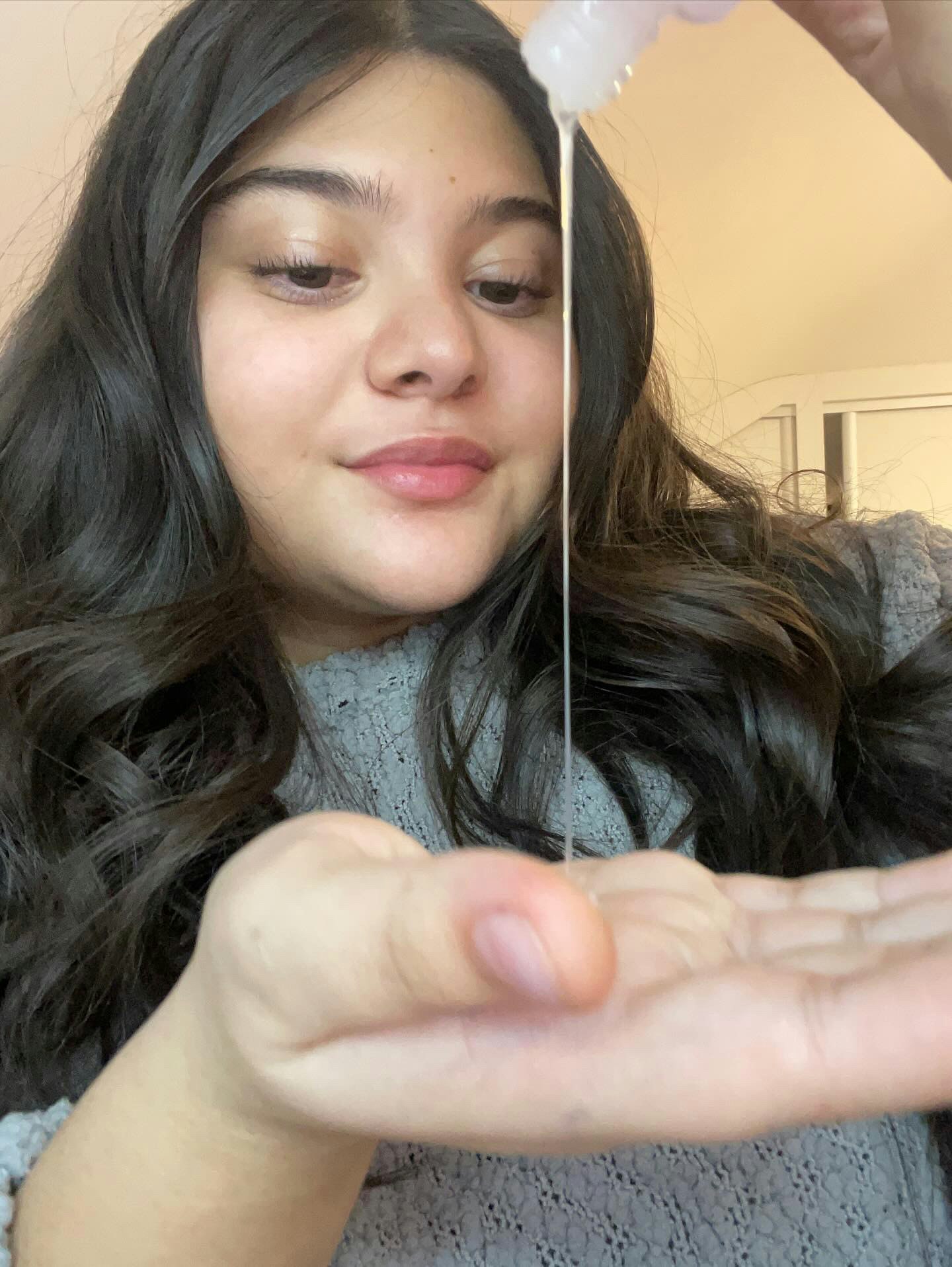 Teenage girl squeezing a serum or moisturiser from a bottle onto her hand.