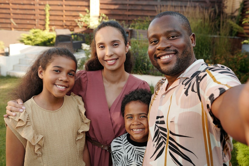 Mother, father, teenage daughter and young child smiling together in a garden.