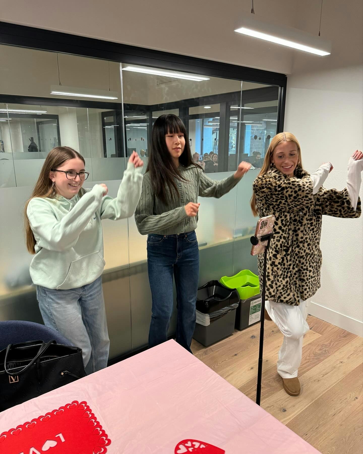 Three teenage girls dancing together in an office-style indoor space.