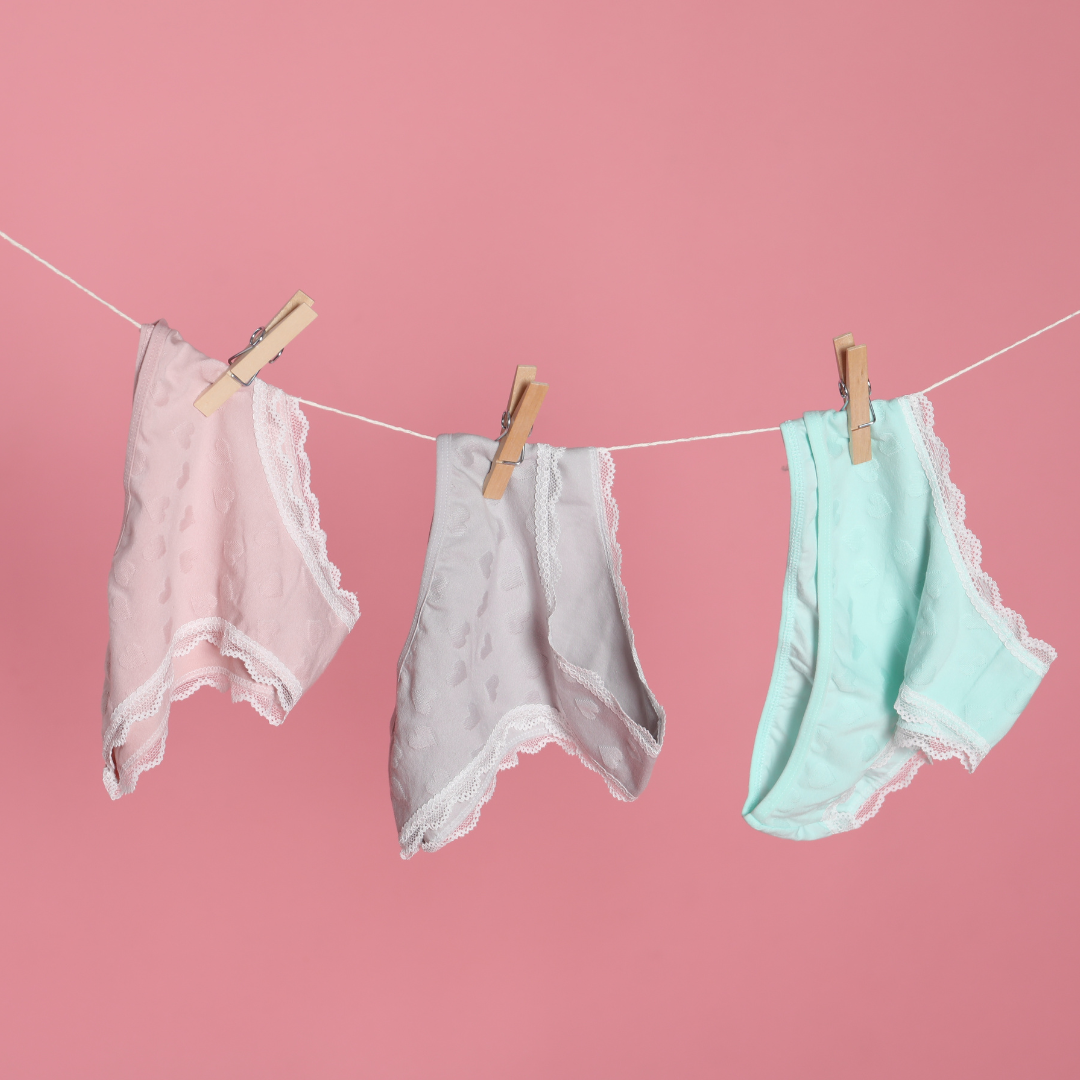 Three pairs of lace-trimmed underwear in pink, grey and mint clipped to a washing line against a pink background.