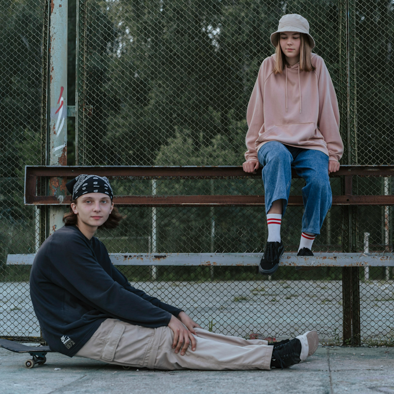 Teenage boy sitting on the ground with a skateboard while a teenage girl sits on a barrier above him at a skate park.