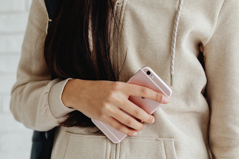 Close-up of a teenage girl in a beige hoodie holding a phone against her chest.
