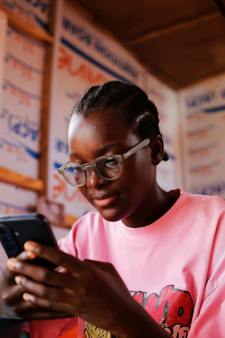 Teenage girl wearing glasses and a pink T-shirt looking down at her phone.