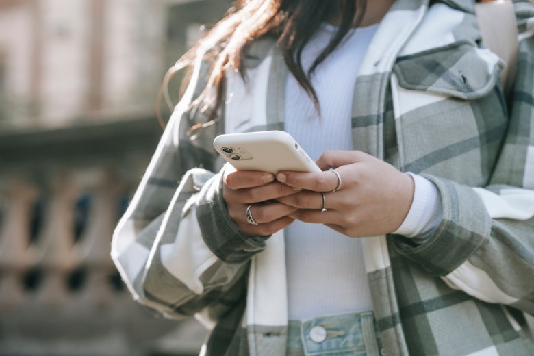 Close-up of a teenage girl's hands holding and typing on a smartphone, wearing a checked shacket.