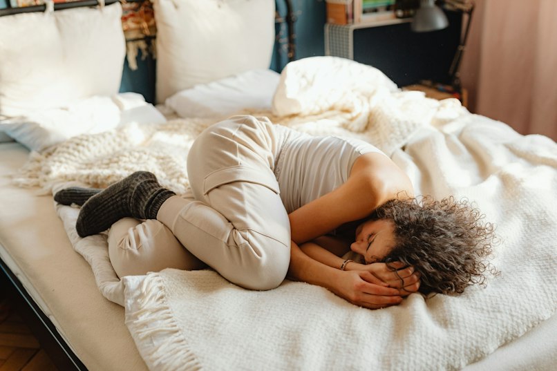 Teenage girl curled up in a fetal position on a bed.