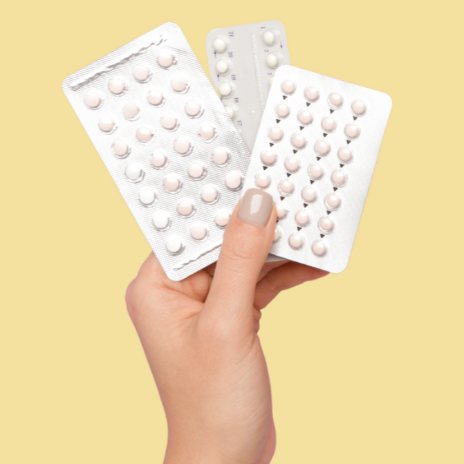 Hand holding three blister packs of contraceptive pills against a yellow background.