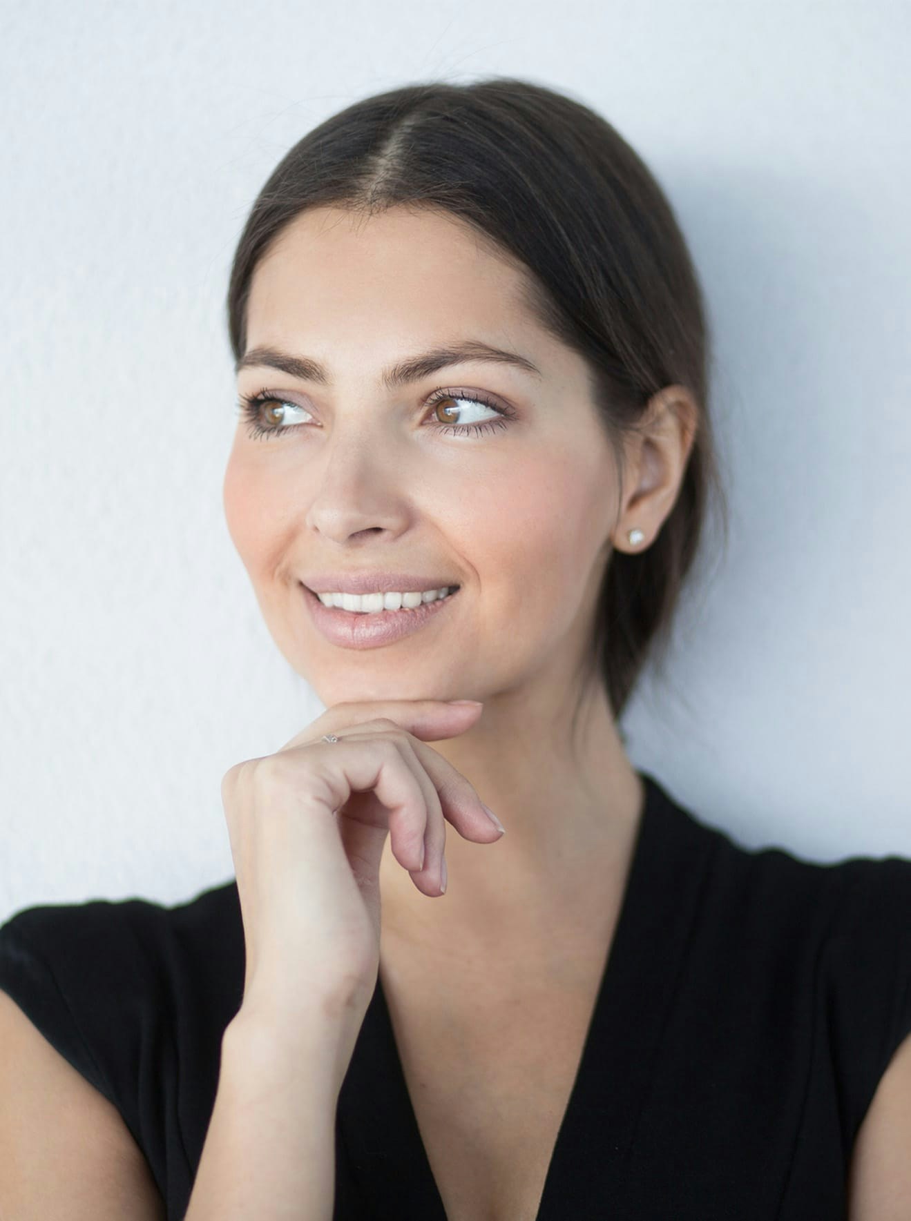Woman in black blouse smiling and holding hand to chin