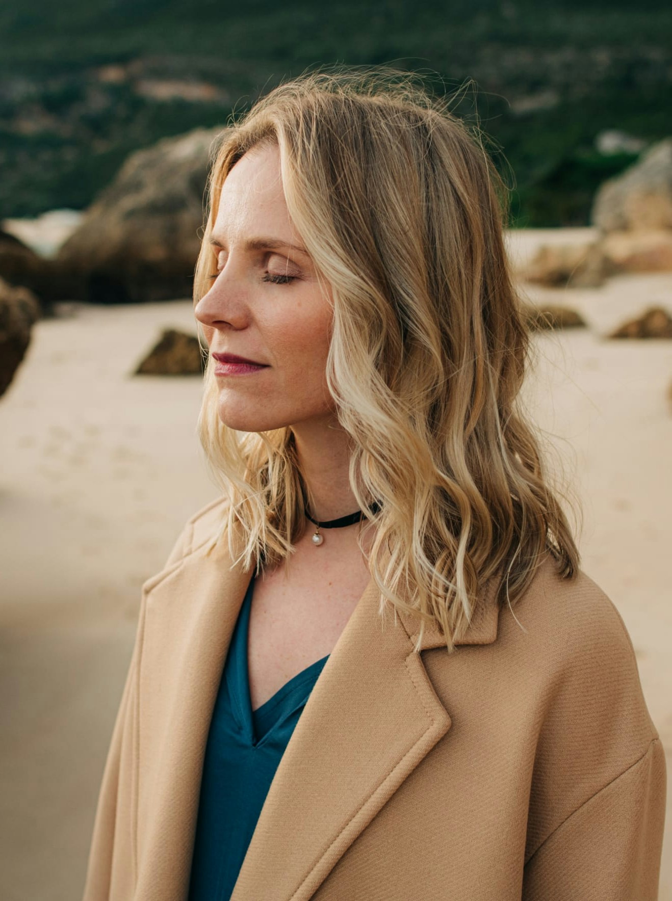 Woman in a coat with her eyes closed, on the beach