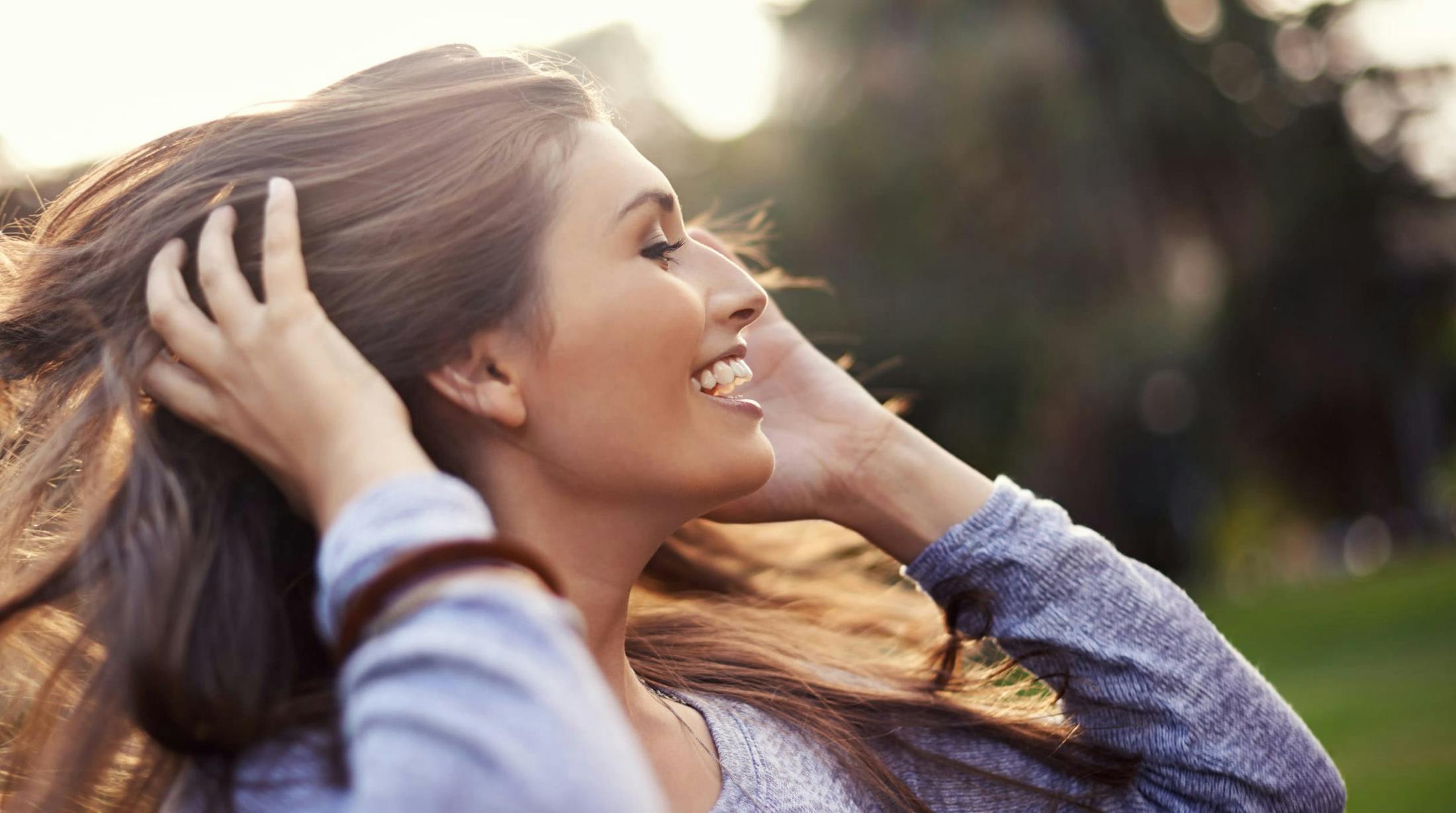 smiling woman with long hair in a park with trees in the background
