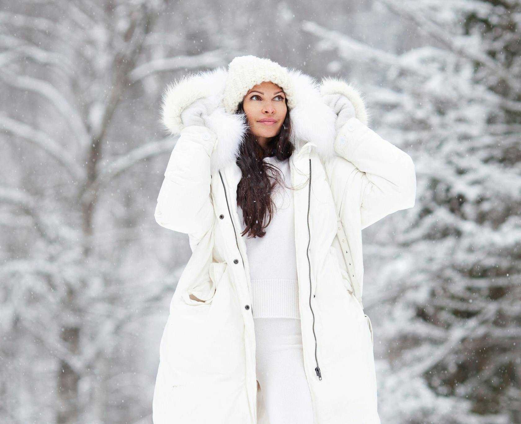 woman in white coat and hat standing in snow