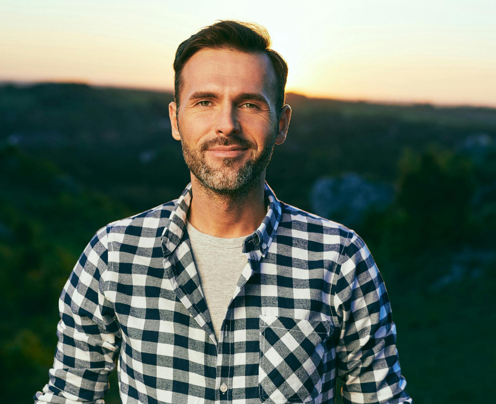 man in a plaid shirt standing in front of a sunset