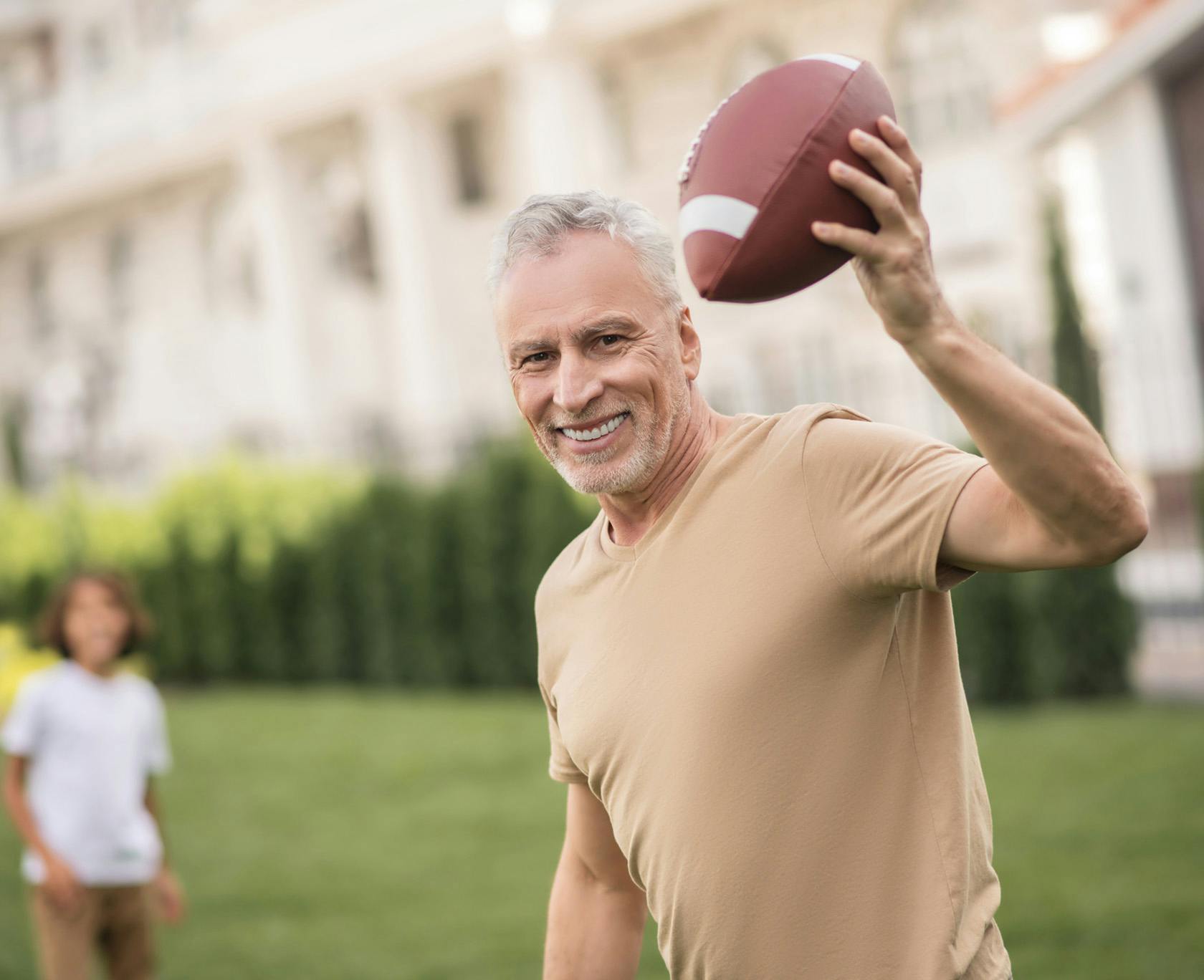 older man throwing a football in a park with a young boy in the background